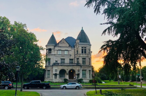 A grand, historic mansion with turrets, surrounded by trees, at sunset.