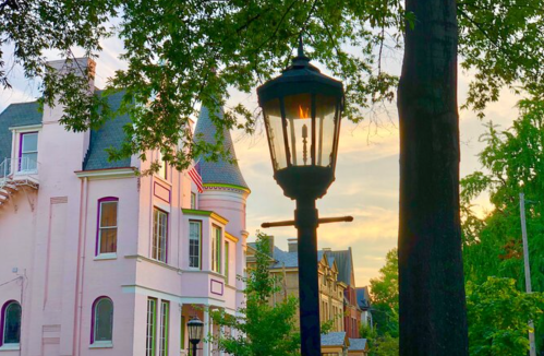 A vintage street lamp in front of a pastel-colored house at sunset, surrounded by trees.