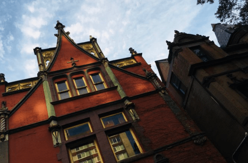 Historic red building with ornate architecture, featuring tall windows and a dramatic sky in the background.