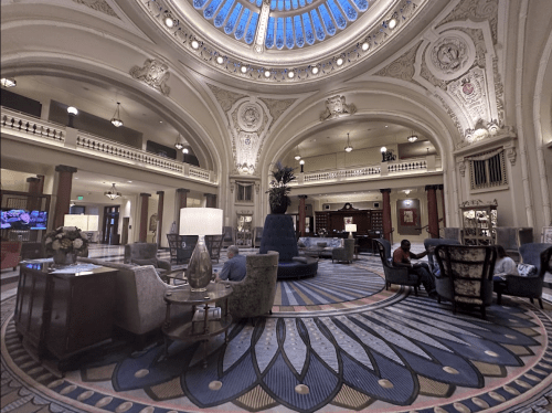 Luxurious hotel lobby with ornate architecture, a large dome, elegant seating, and decorative rugs.