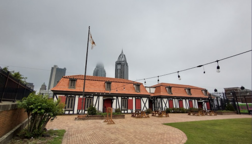 A historic building with a red-tiled roof and wooden accents, surrounded by a courtyard and city skyline in the background.