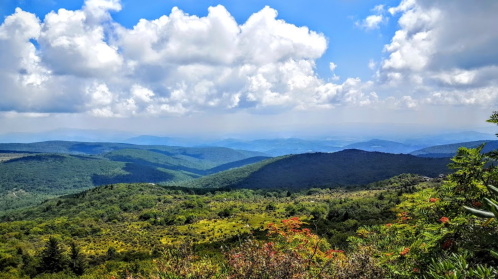 A panoramic view of rolling green hills under a partly cloudy sky, with distant mountains fading into the horizon.