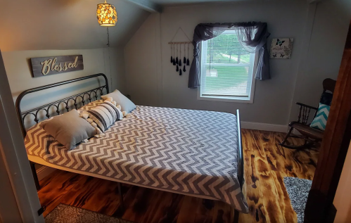Cozy bedroom with a metal bed, chevron-patterned bedding, a rocking chair, and a "Blessed" sign on the wall.