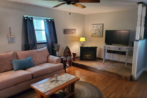 Cozy living room with a pink sofa, TV, lamp, and a decorative fireplace on a wooden floor.