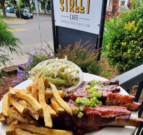A plate of ribs with barbecue sauce, fries, and coleslaw in front of a café sign.