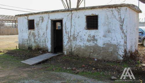 Abandoned building with a weathered white exterior, barred windows, and a sloped entrance ramp.