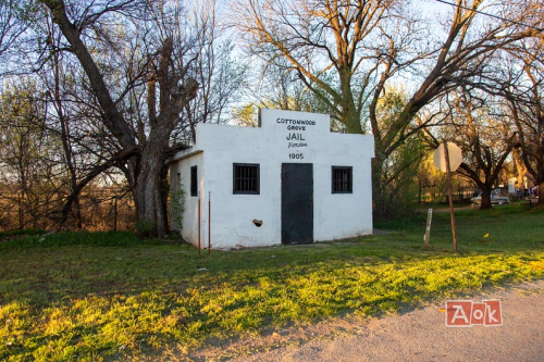 Historic white jail building with barred windows, surrounded by trees, labeled "Cottonwood Grove Jail, 1905."