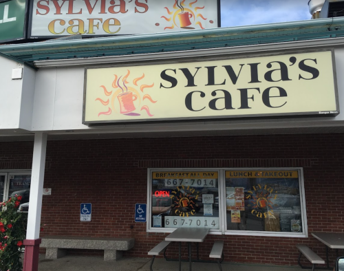 Exterior of Sylvia's Cafe, featuring a sign with the cafe's name and a "Breakfast All Day" banner. Open for lunch and takeout.