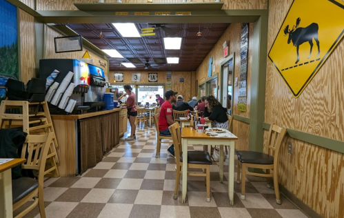A cozy restaurant interior with wooden decor, checkered floors, and diners enjoying meals at tables.