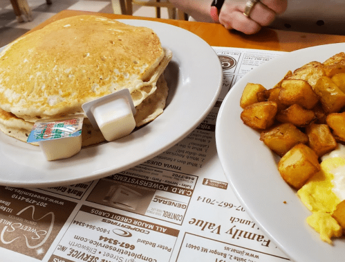 A plate of fluffy pancakes with syrup and a side of golden-brown breakfast potatoes.