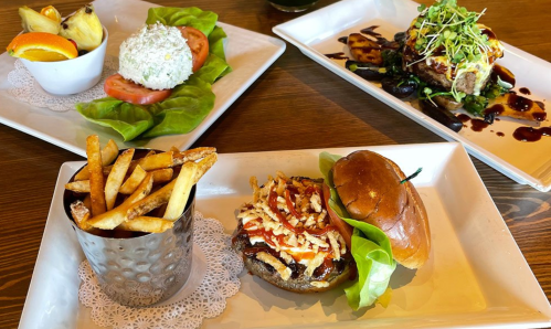 A plate with a burger topped with sauce and crispy onions, fries in a cup, and a salad with tomatoes and rice.