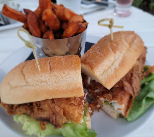 A plate featuring two fried chicken sandwiches with lettuce, served alongside a cup of sweet potato fries.