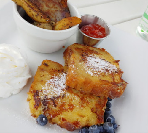 A plate with two pieces of French toast, blueberries, whipped cream, and a side of seasoned potatoes with ketchup.