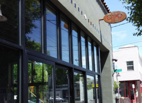 Exterior of a building with large windows and a sign that reads "CURO," surrounded by trees and a street view.