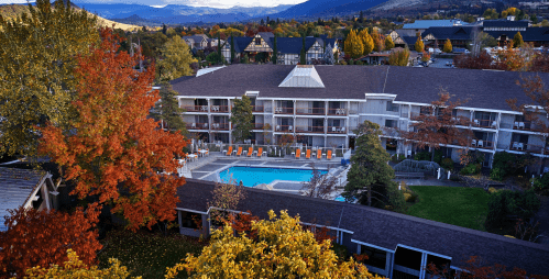 Aerial view of a hotel with a pool surrounded by autumn trees and mountains in the background.