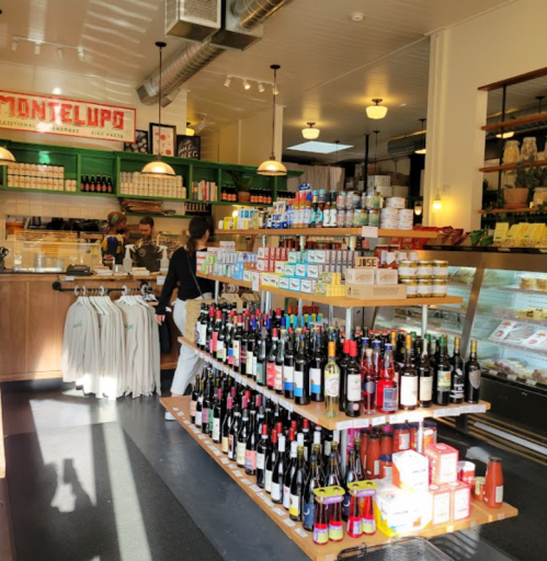 A vibrant store interior with shelves of wine, groceries, and a counter with staff serving customers.