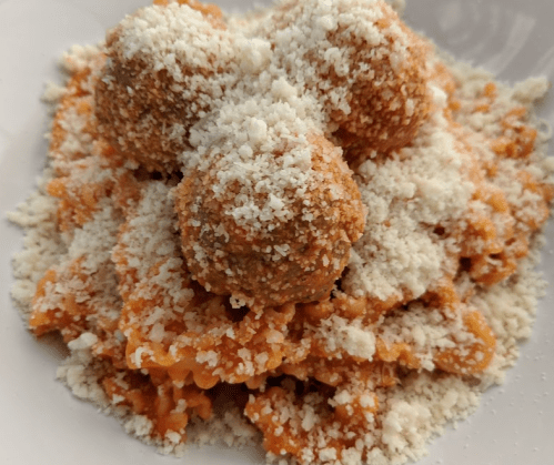A plate of pasta topped with three meatballs and sprinkled with grated cheese.