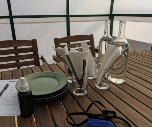 Table set with green plates, glasses, utensils, and water bottles in a cozy, tent-like setting.