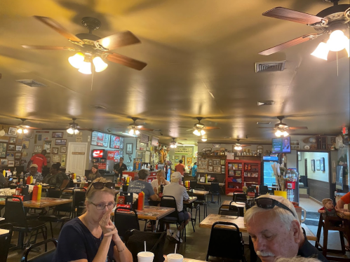 A bustling diner interior with ceiling fans, tables, and patrons enjoying their meals amidst wall decor and memorabilia.