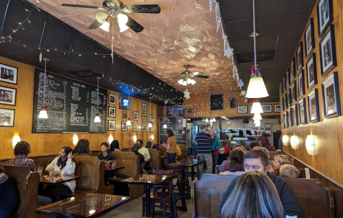 A bustling café with patrons seated at wooden tables, walls adorned with photos, and warm lighting creating a cozy atmosphere.