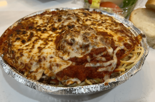 A foil container filled with spaghetti topped with marinara sauce and melted cheese, alongside a salad and bread.
