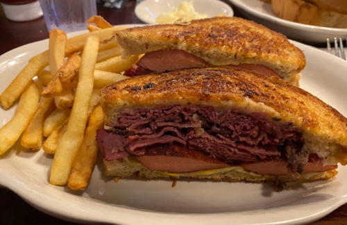 A close-up of a toasted sandwich filled with layers of meat, served with a side of golden French fries.