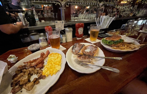 A table with two plates of breakfast and lunch, featuring eggs, bacon, toast, a burger, fries, and drinks.