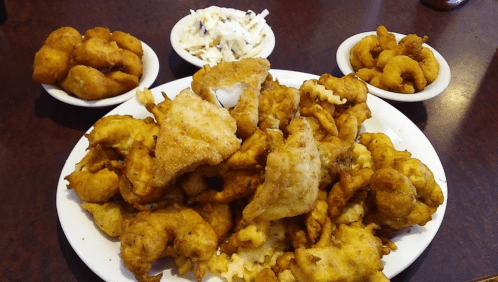 A large platter of golden fried fish and seafood, accompanied by three small bowls of coleslaw and fried snacks.