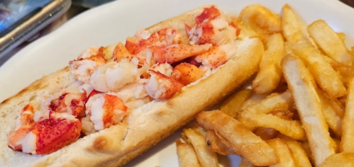 A lobster roll filled with lobster meat served alongside a side of crispy French fries.