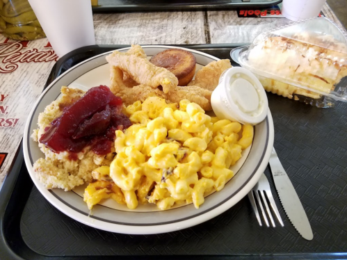 A plate of food featuring macaroni and cheese, fried chicken, cornbread, and a dessert, served on a tray.