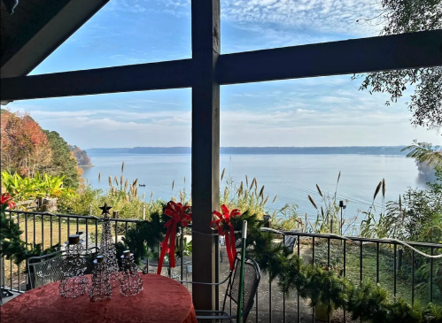 A serene lakeside view from a covered porch, decorated with holiday wreaths and a festive table setting.