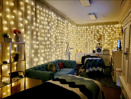 A cozy room with a blue couch, soft blankets, and walls adorned with warm string lights.