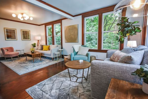 Cozy living room with large windows, modern furniture, and a mix of soft colors and textures.