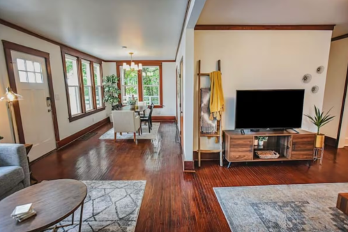 Cozy living room with wooden floors, a TV, and a dining area with large windows and modern decor.