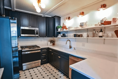 Modern kitchen with dark cabinets, stainless steel appliances, white countertops, and open shelving displaying dishware.