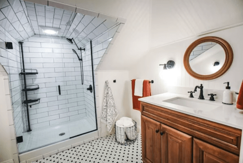 Modern bathroom featuring a glass shower, wooden vanity, round mirror, and black and white tile flooring.