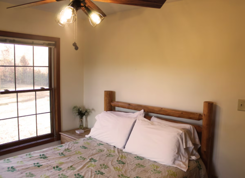 Cozy bedroom with a wooden bed, white pillows, and a window showing a view of nature outside.