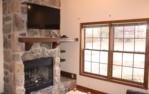 Cozy living space featuring a stone fireplace, a mounted TV, and a large window with a view outside.