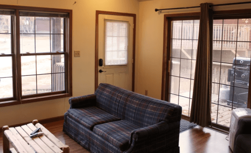 Cozy living room with a plaid sofa, large windows, and a door leading to an outdoor area.