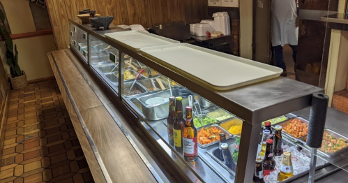 A buffet counter with various food trays and drinks, set in a casual dining environment.