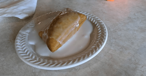 A golden pastry drizzled with icing on a white plate, resting on a light-colored table.
