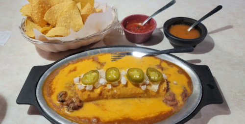 A sizzling plate of enchiladas topped with cheese and jalapeños, served with tortilla chips and two sauces.