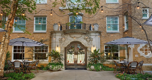 Charming outdoor dining area with tables, umbrellas, and string lights in front of a brick building entrance.