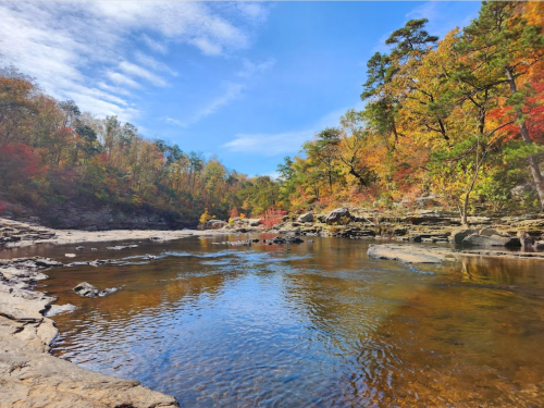 A serene river scene surrounded by colorful autumn foliage and clear blue skies.