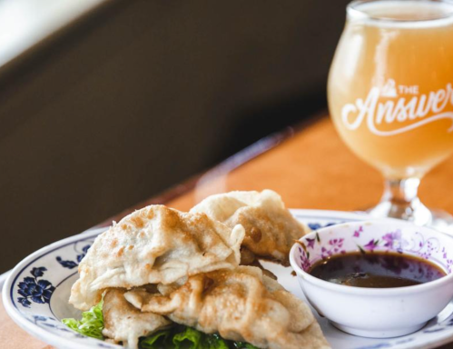 A plate of crispy dumplings with a side of dipping sauce, accompanied by a glass of beer.