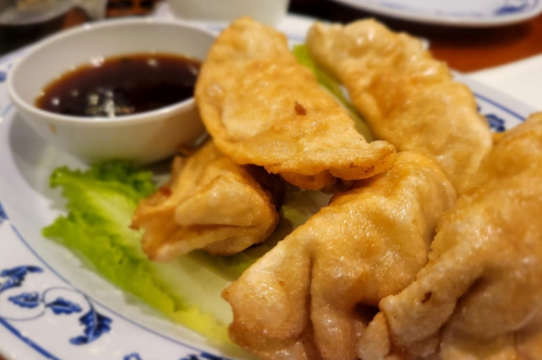 A plate of golden fried dumplings served with a small bowl of dipping sauce and lettuce leaves.