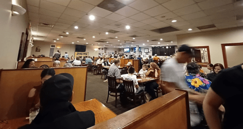 A busy restaurant filled with diners at tables, with a lively atmosphere and people moving around.