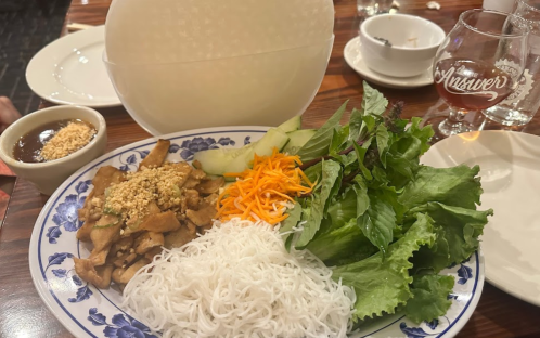 A plate of fresh vegetables, rice noodles, and grilled chicken topped with peanuts, served with a dipping sauce.