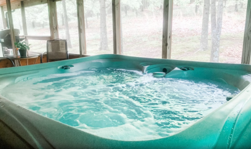 A hot tub filled with bubbling water, set in a screened-in area surrounded by trees.