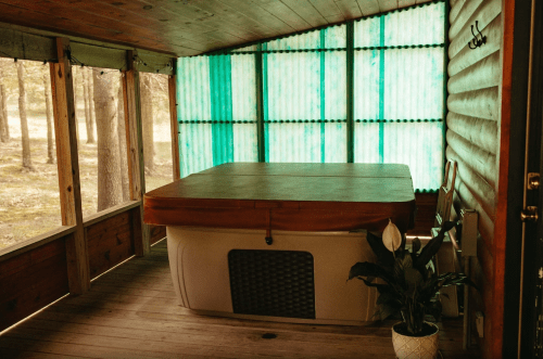 A cozy screened porch with a hot tub, wooden walls, and a potted plant, surrounded by trees.